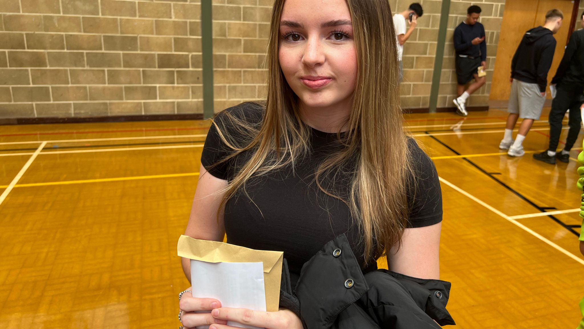 Scarlett wearing black t-shirt with results standing in school hall.