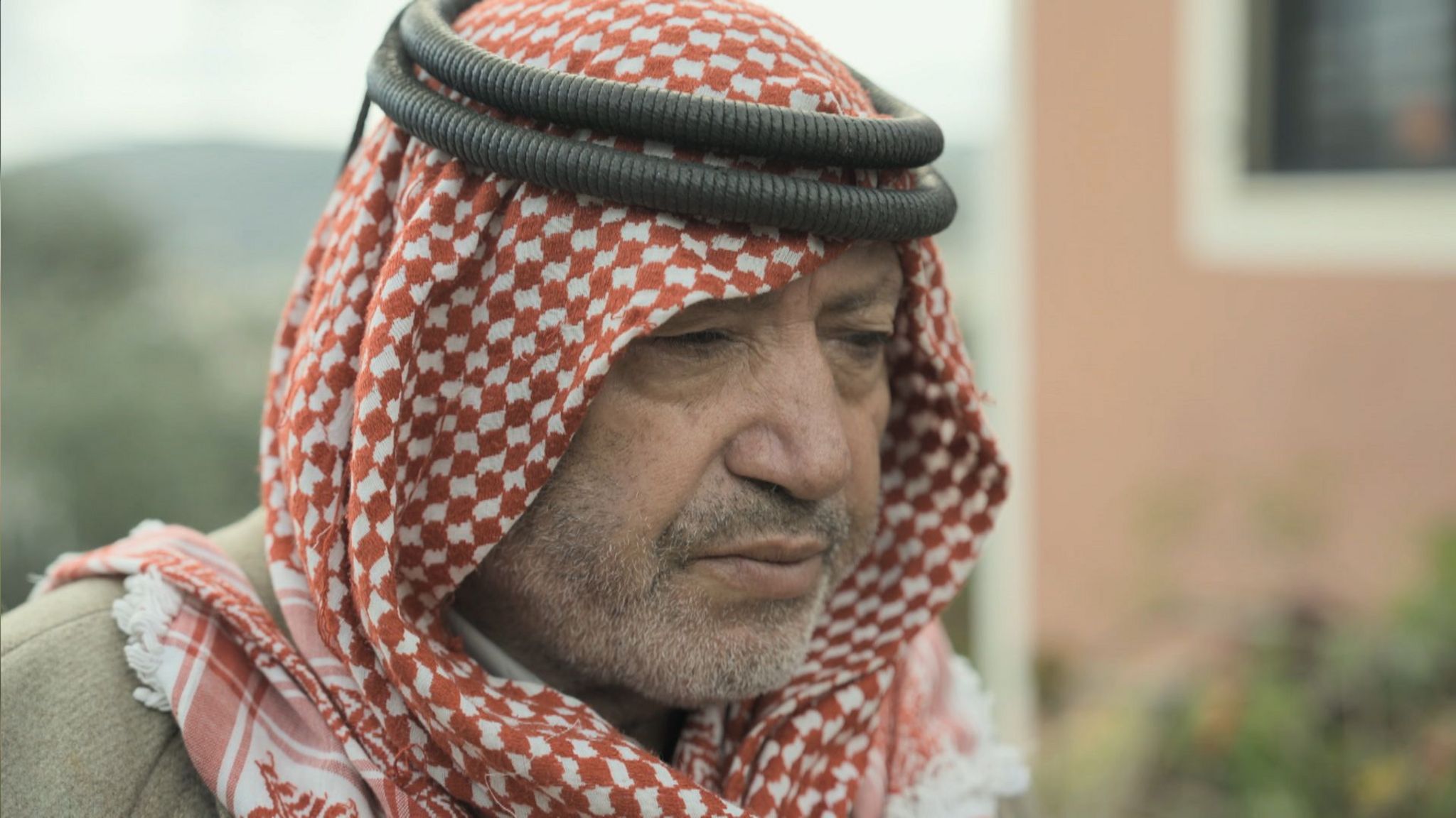 Nabil in a red and white checked headdress looking pensively at the floor 