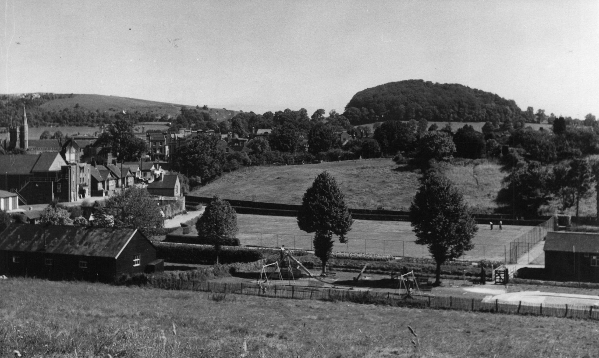 Black & white view of the park from top of a hill, looking down to see the park among fields and a street of homes