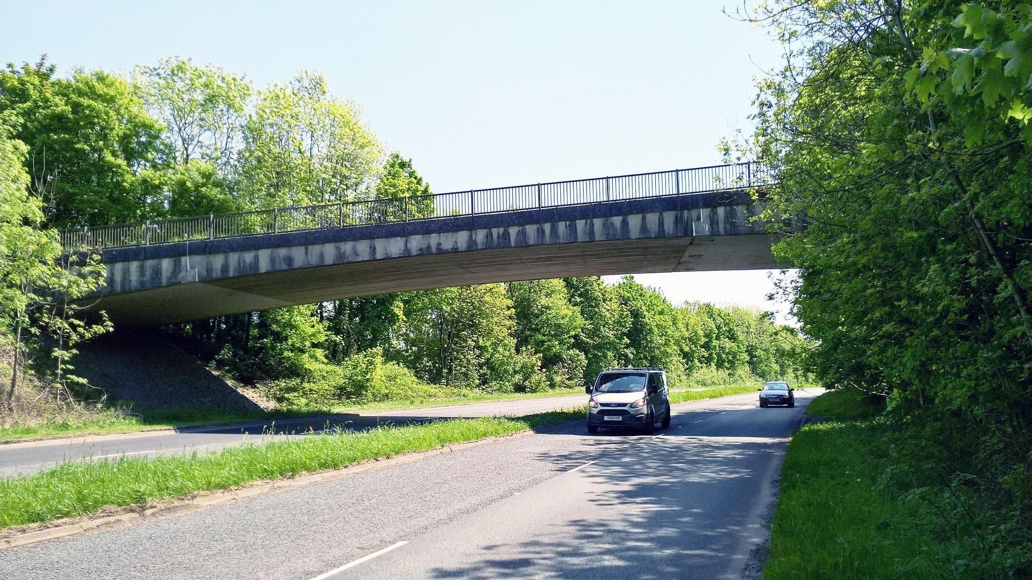 Van and car driving underneath 1970s style bridge going over main road