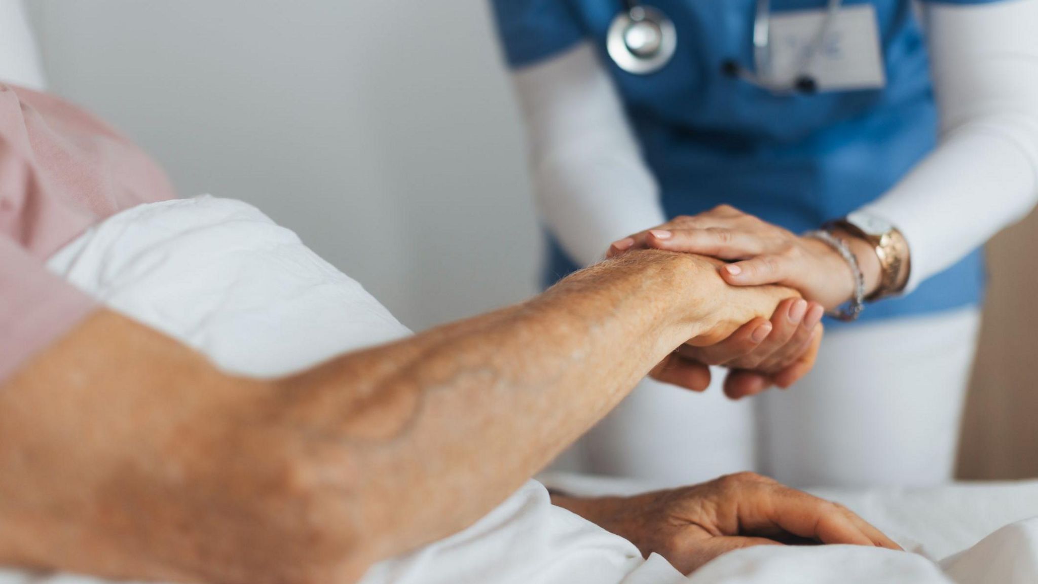 Close-up of caregiver holding senior client hand. Support from nurse to patient, taking care of elderly man in hospital. Emotional support and care in healthcare, hospice care.