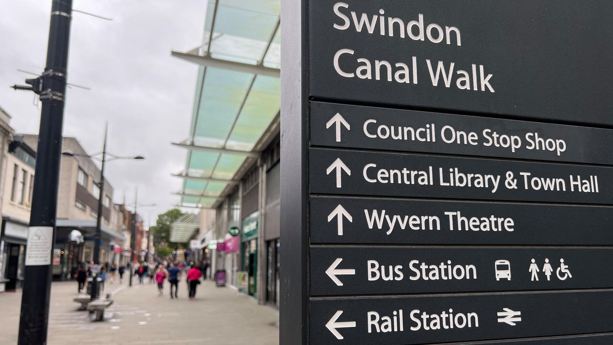 View of a sign on Canal Walk in Swindon with the town centre behind it