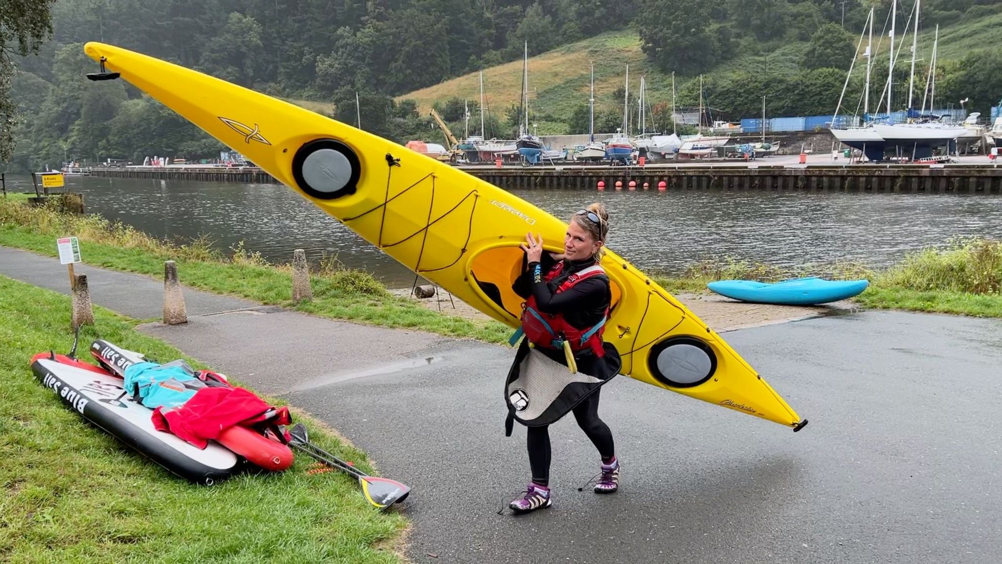 Kerri Adams in a wetsuit carrying a yellow canoe on land