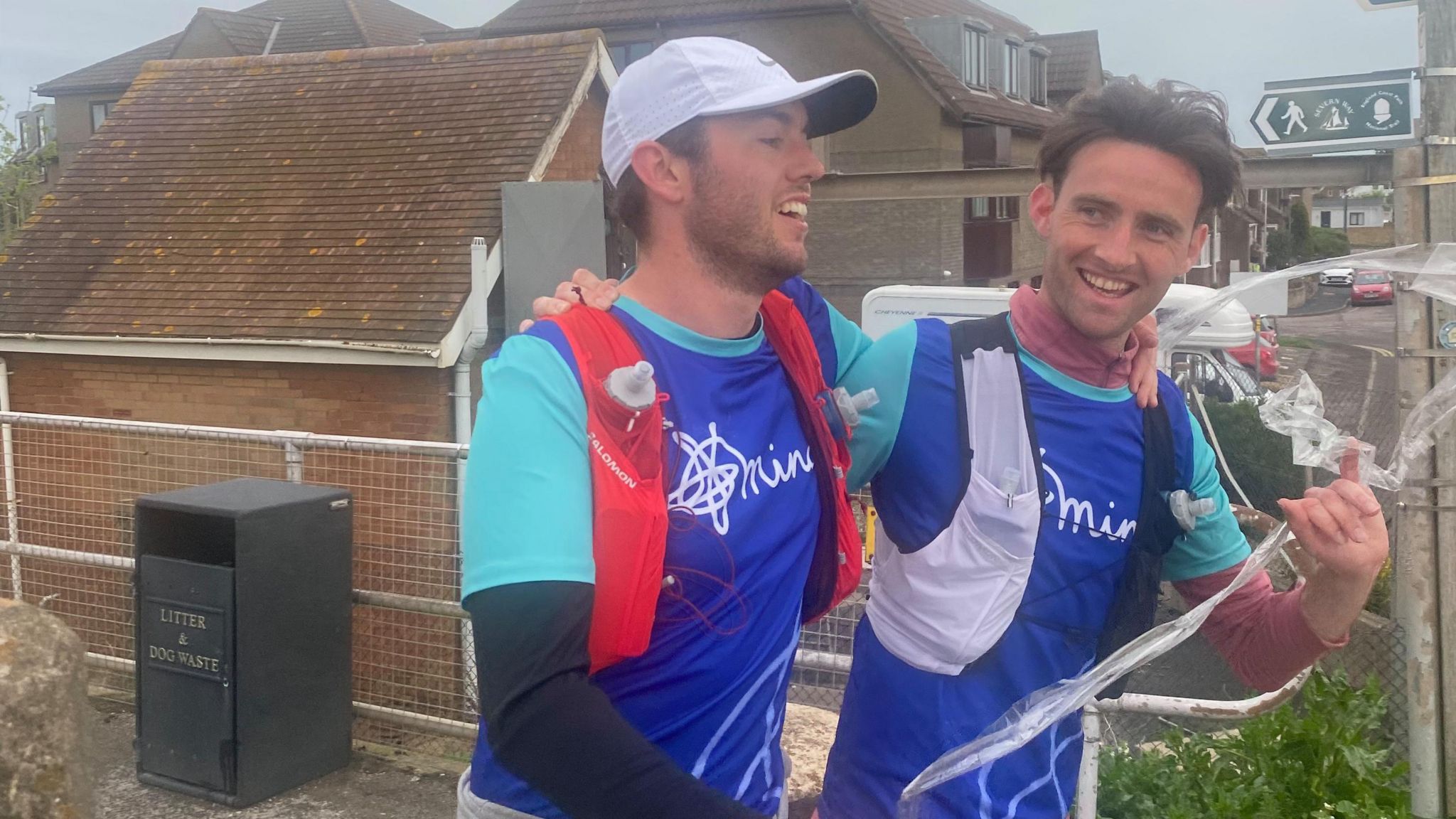 Tom and Cameron, dressed in running clothes have their arms around eachother as they run. They are smiling and wearing vests with the Mind logo on them