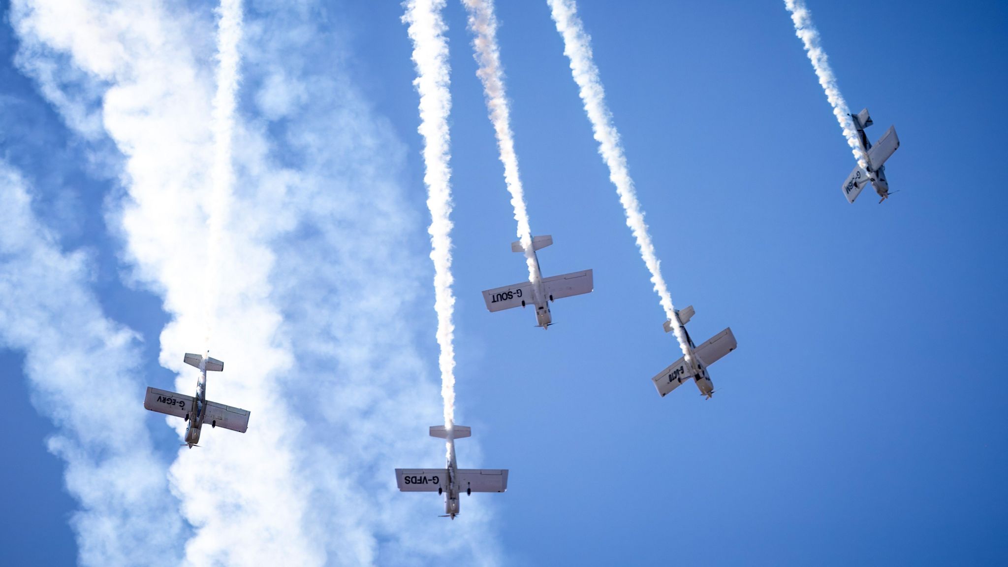 Five grey planes spiral downwards, leaving trails of white smoke behind them