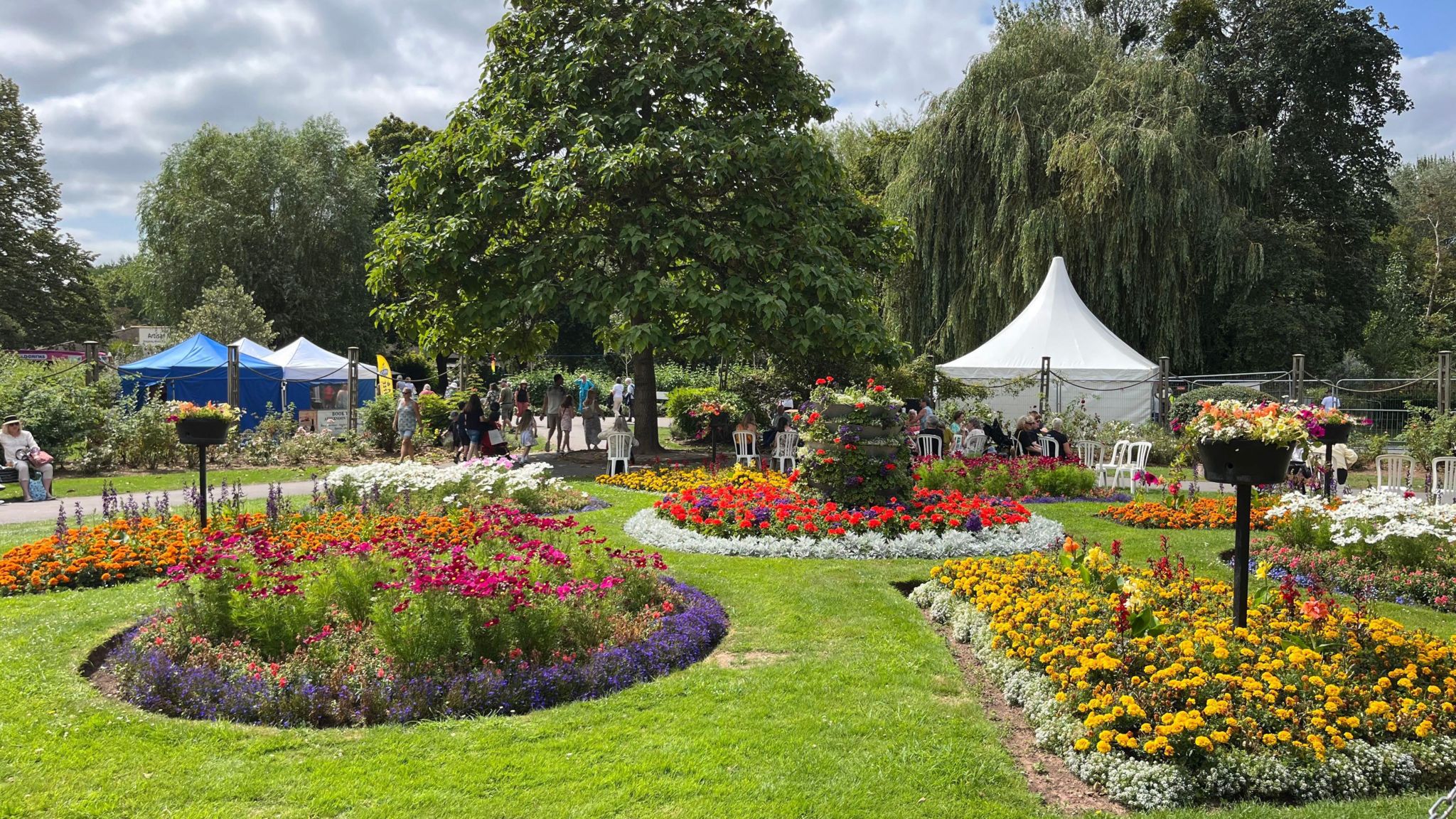 Taunton Flower Show. There are many different flower beds and people hanging around the area. 