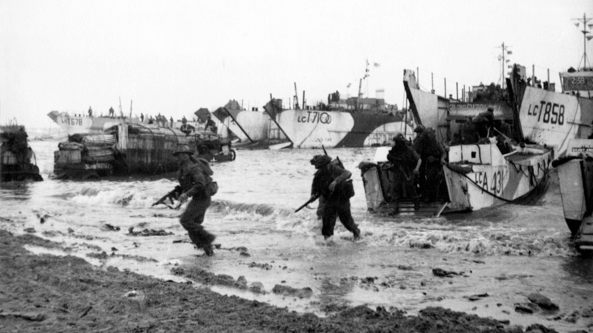 Black and white image showing troops emerge from landing craft on a Normandy beach during the invasion of France on 6 June, 1944 