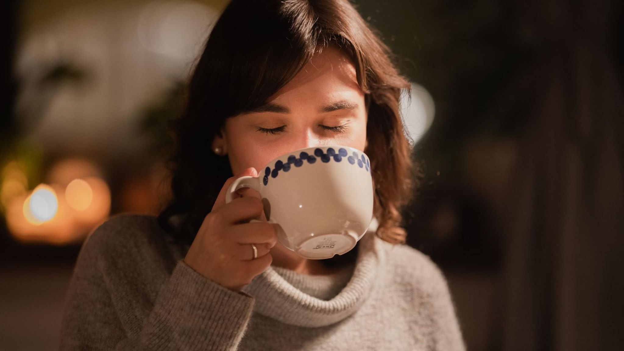 Young woman enjoying a warm drink from an oversized mug providing as much comfort as her natty jumper.