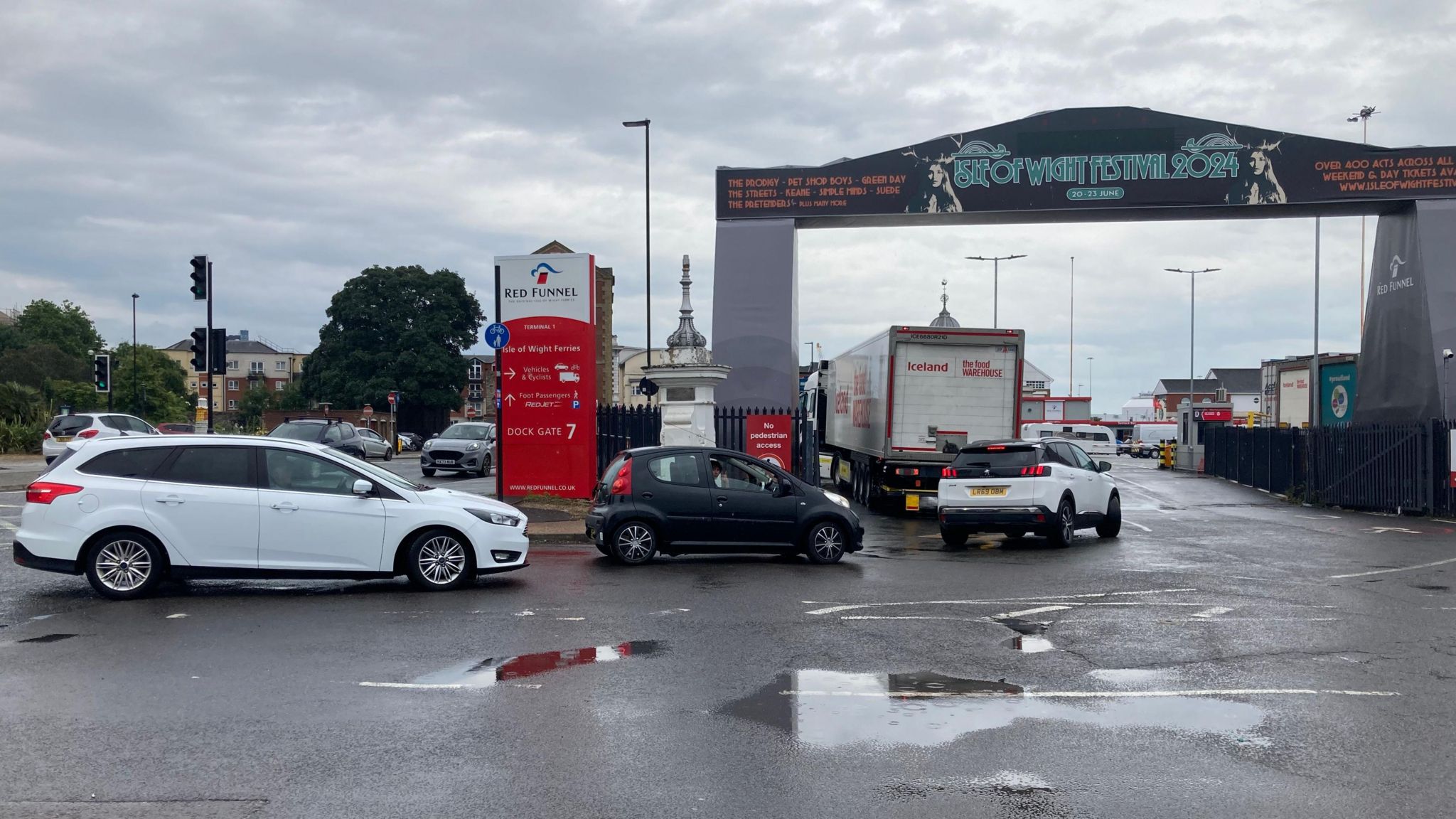 Southampton Red Funnel ferry terminal entrance for cars, a white car, small black car and black and white car queue behind an Iceland lorry to get through the entrance. There is a Red Funnel sign in the background.