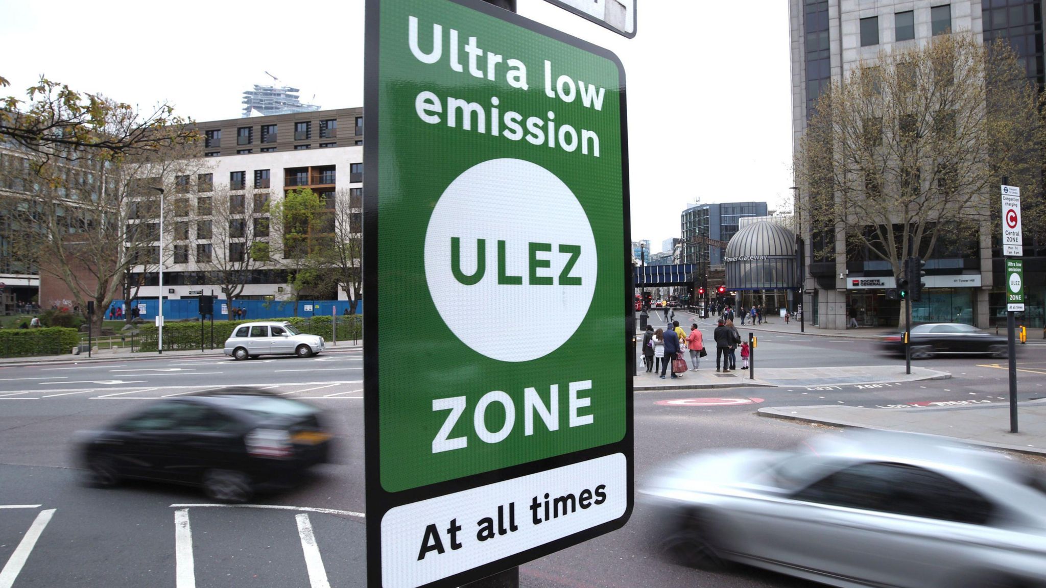 Green and white Ulez zone sign in foreground, cars in background at Tower Hill in central London 