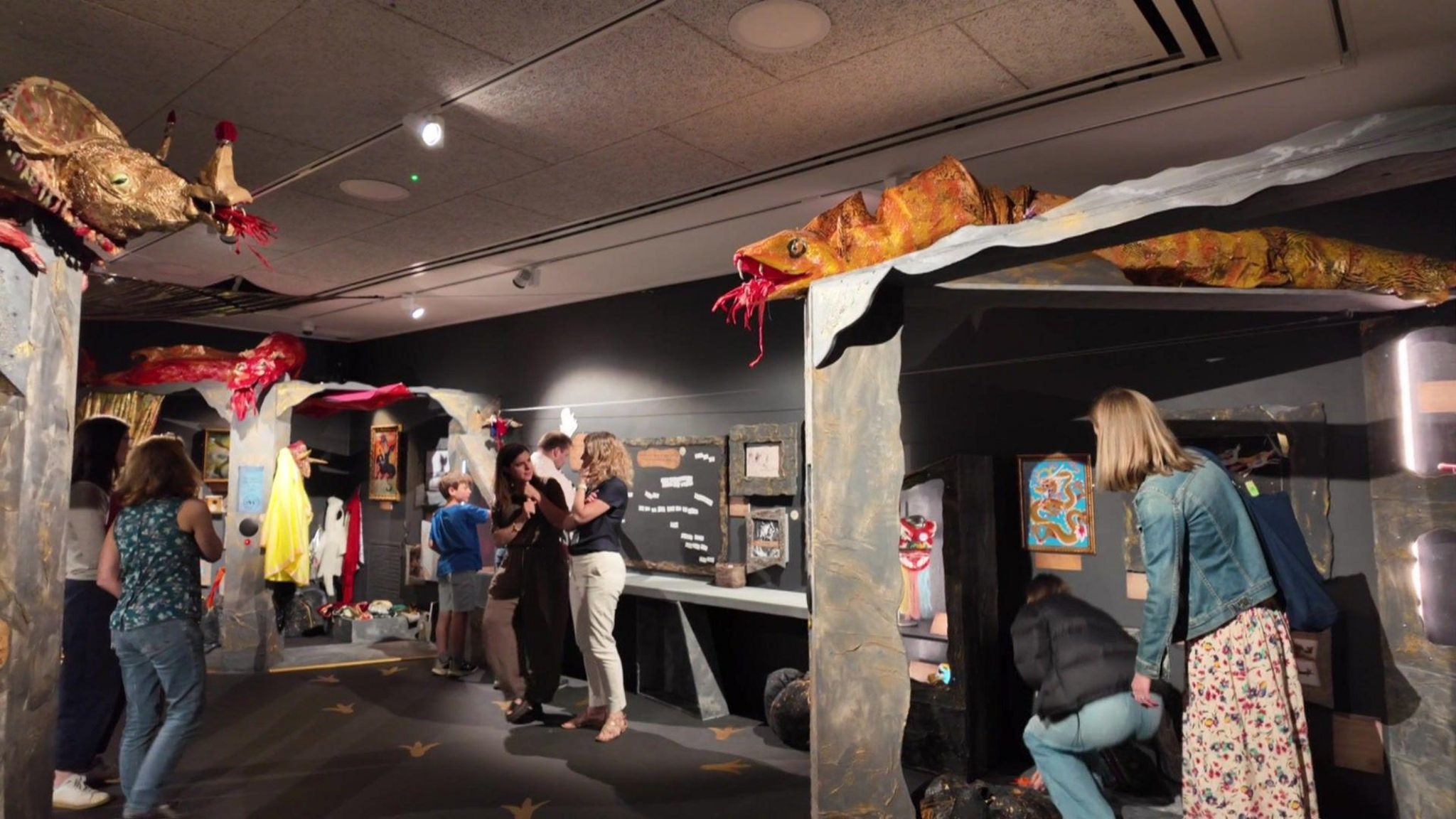 People watching the dragons in the museum's exhibition. Some are walking around and some are standing, having a conversation. A boy could also be seen in the distance.