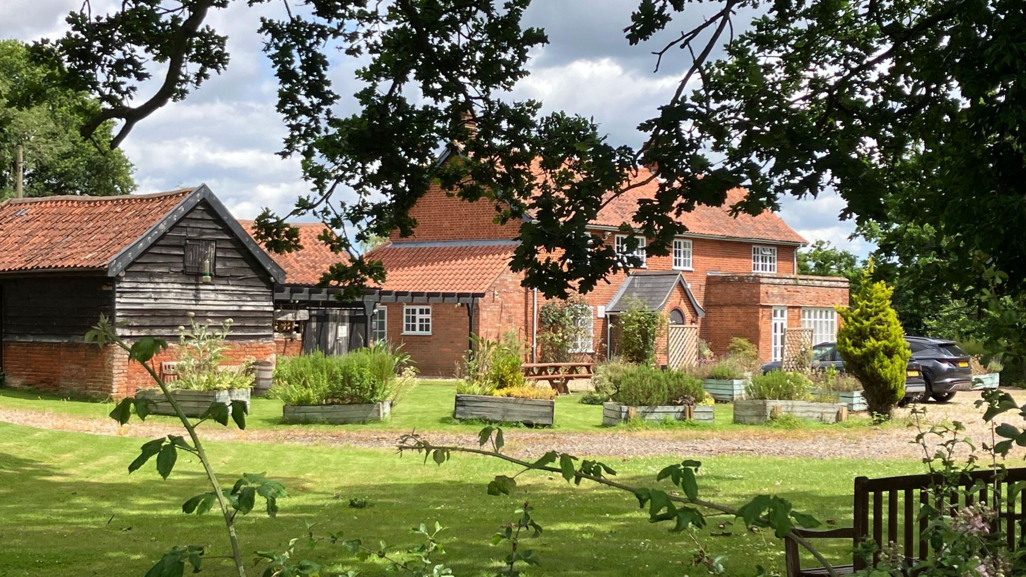 The brick facade of the former pub framed by trees and bushes and a green lawn 