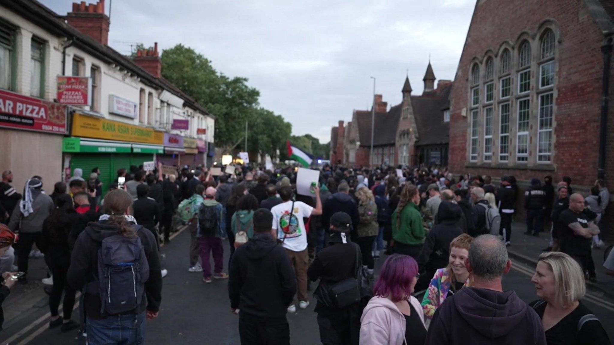 The back of a crowd of counter-protesters in a street, holding signs and speaking to one another