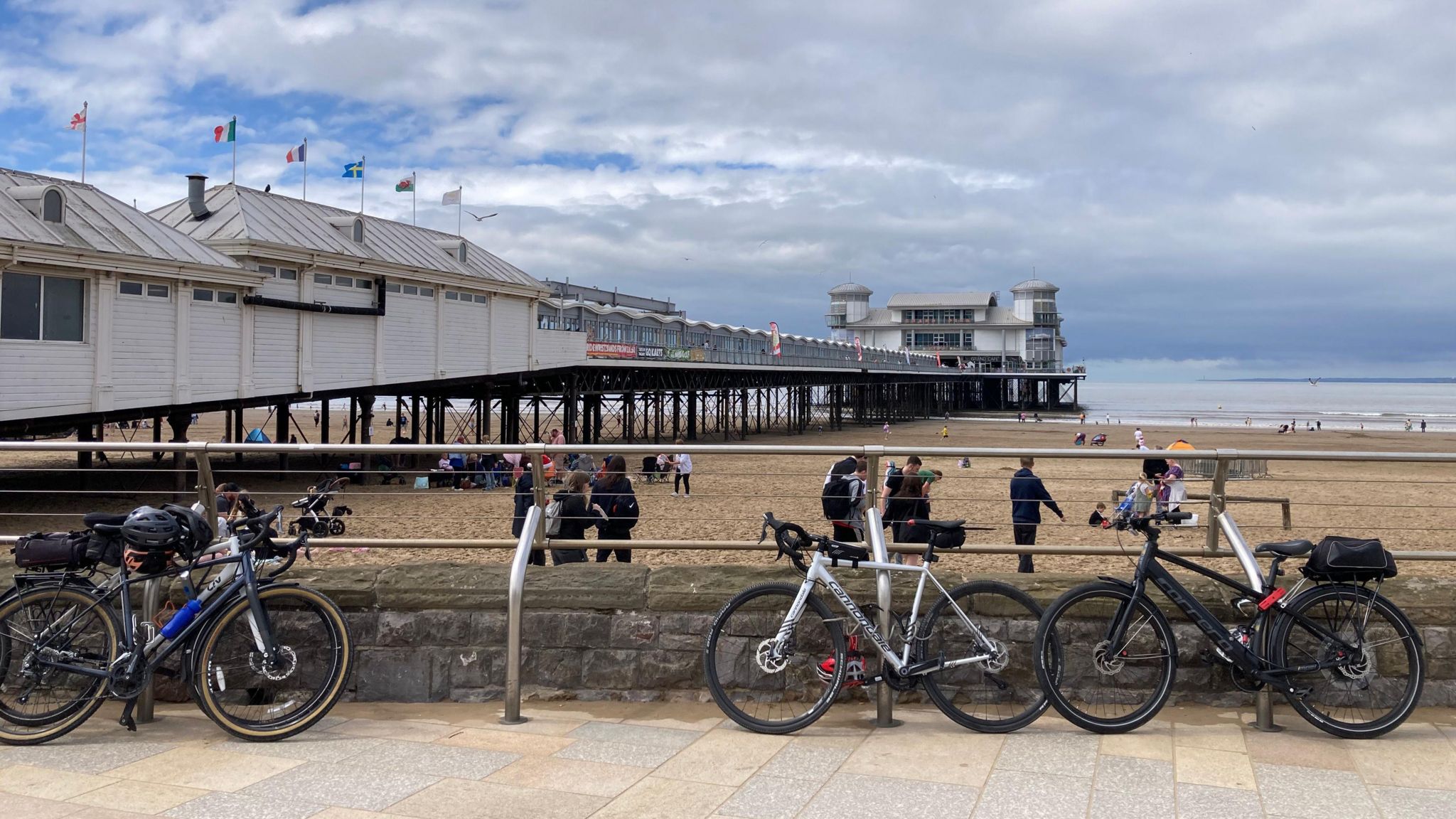 Three bicycles on racks in front of a beach front and a pier