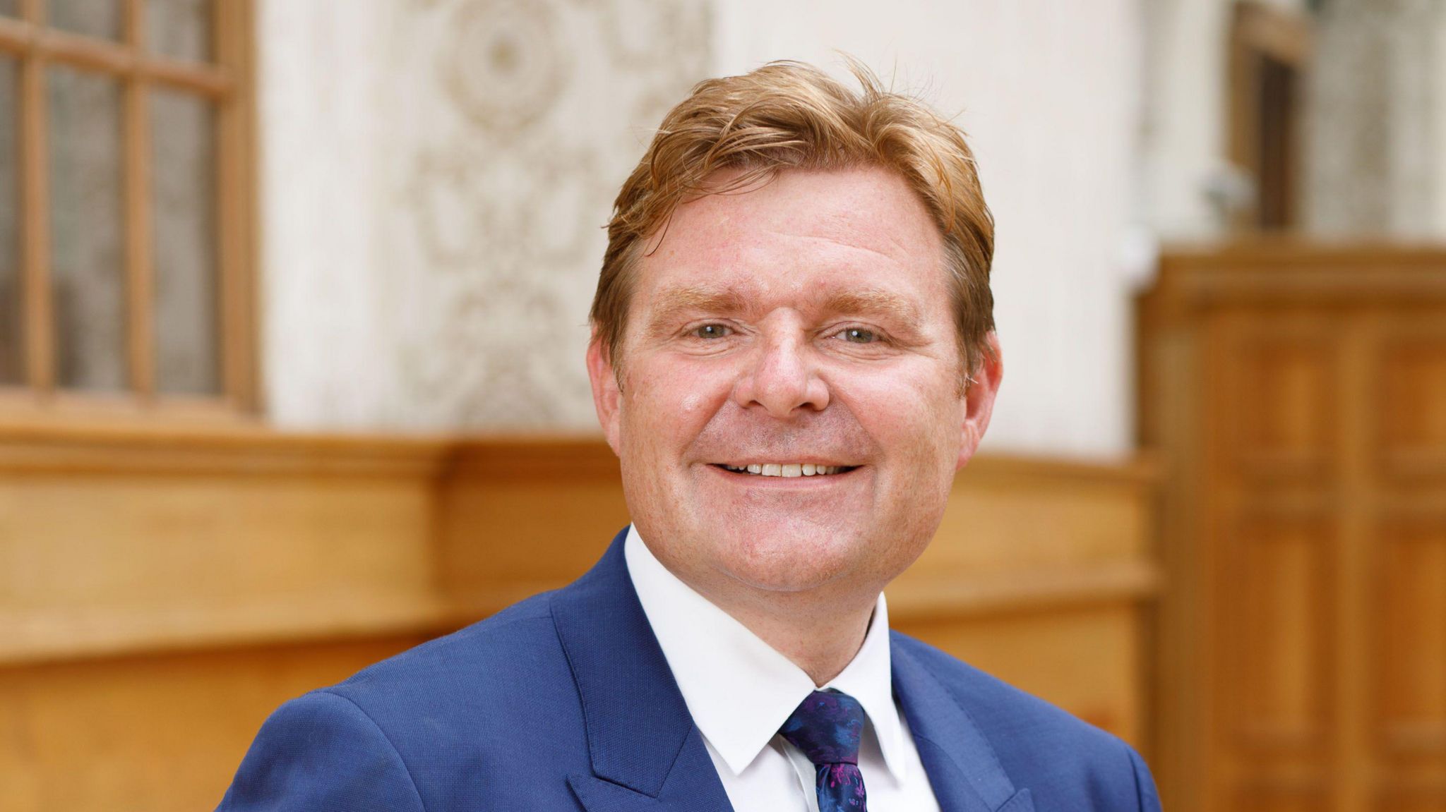 John Cotton wearing a blue suit, white shirt and navy blue tie