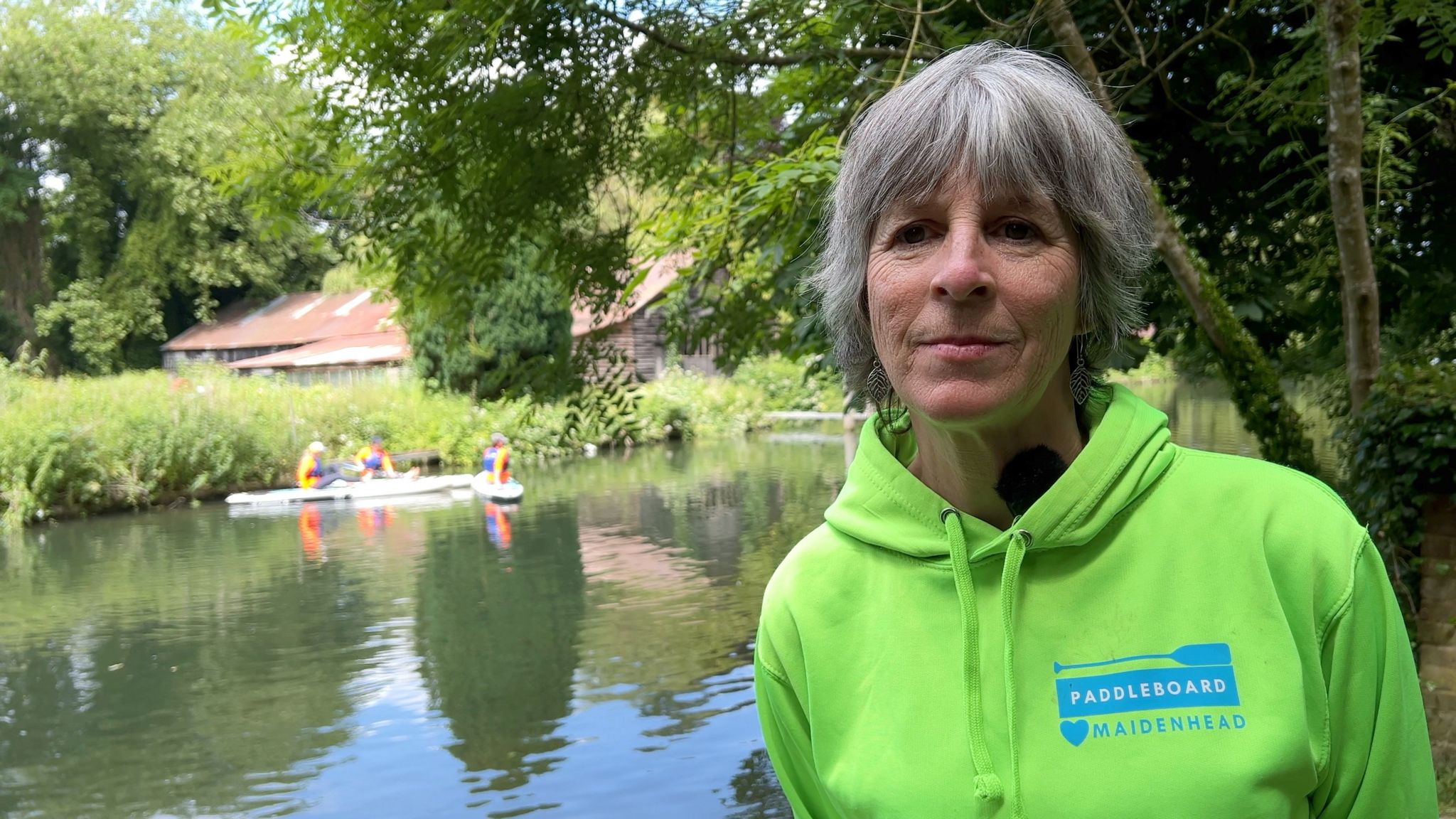 Tara Crist stands on the banks of the Thames with paddle-boarders from the school she runs on the river behind her