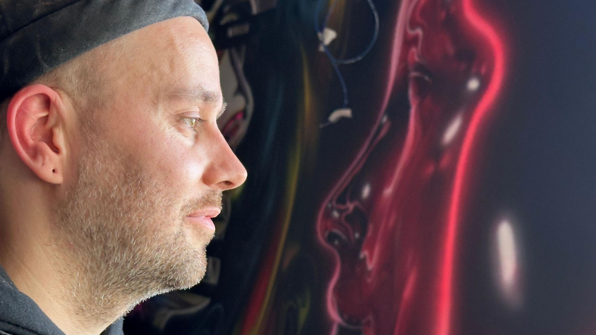Spray paint artist Daniel Russell-Ahern staring at a red face he has painted in Snobs