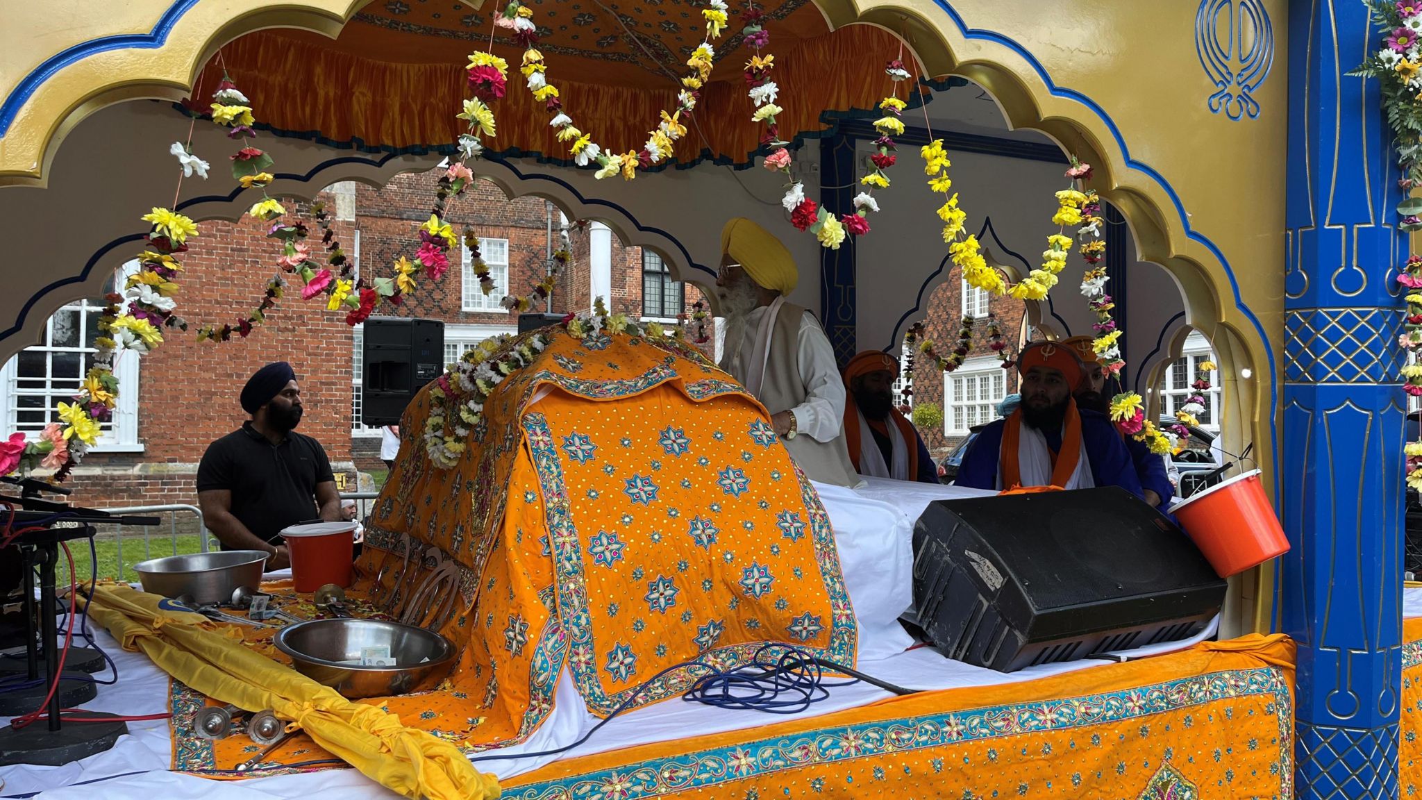 A float with flowers and orange cloth, holding a holy Sikh book