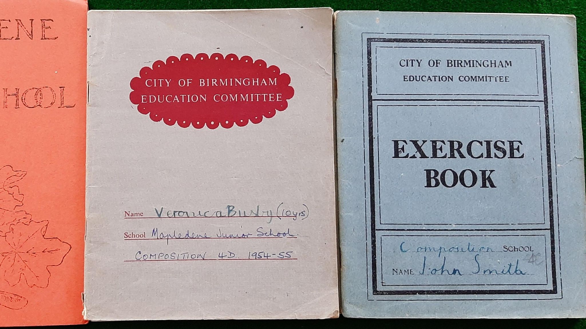 A white school exercise book and a blue school exercise book, with children's names handwritten on the front.