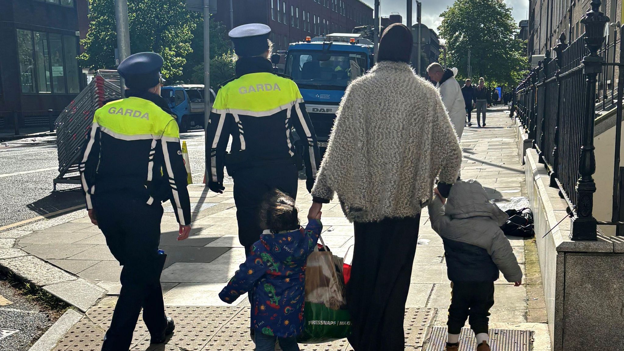 A woman walks with two children escorted by gardaí