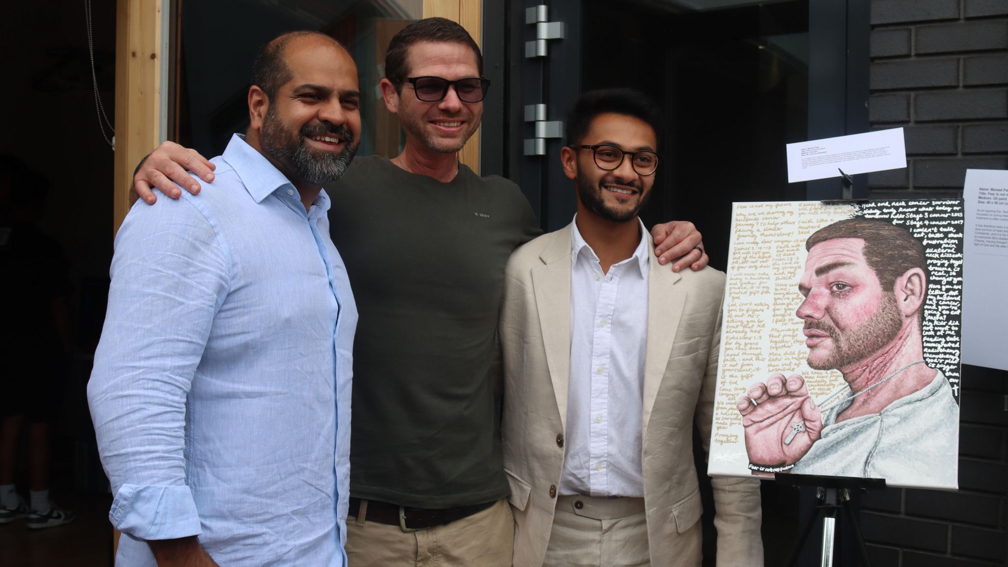 Three men pose for photo next to a piece of art looking happy. 