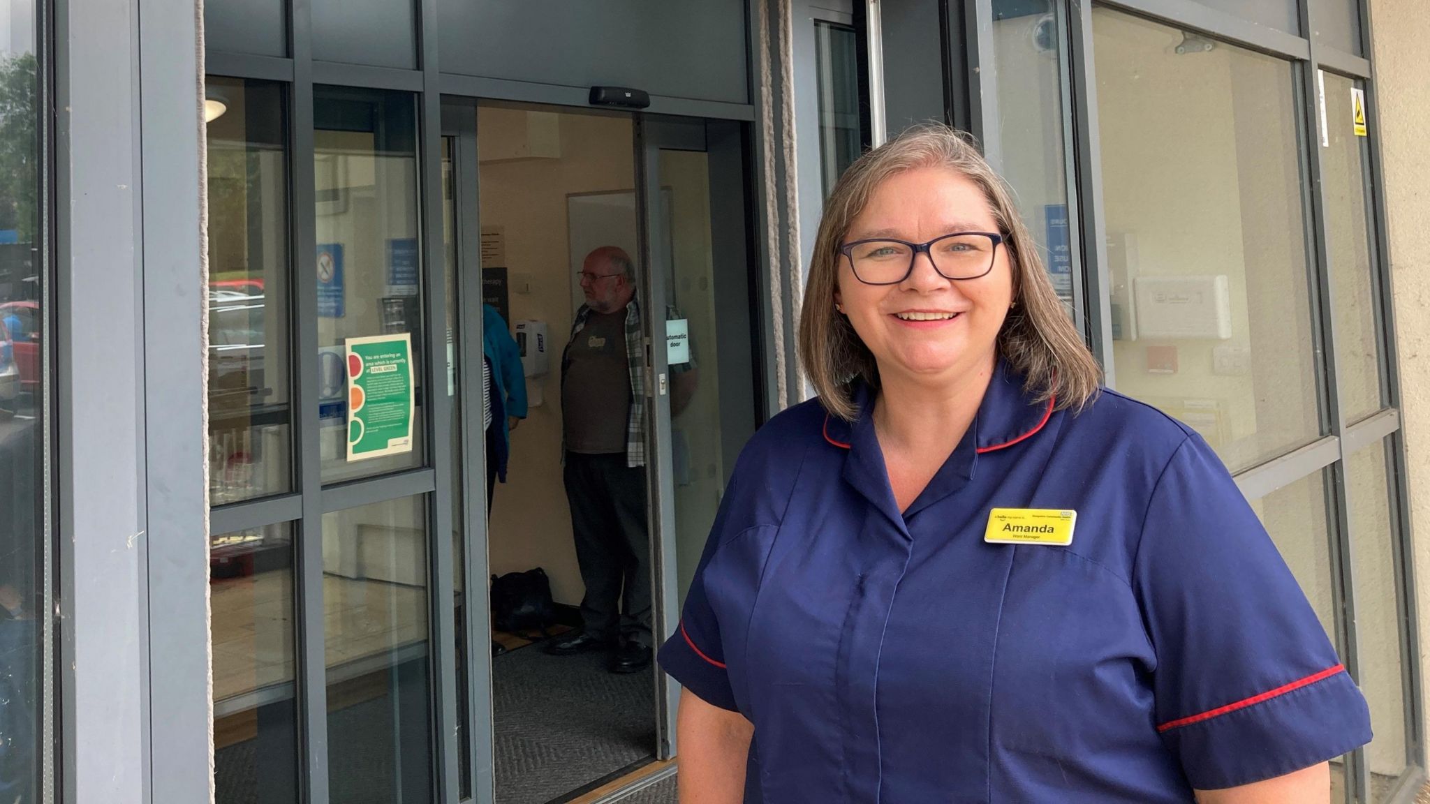 Ward manager Amanda Houghton wearing a dark blue uniform and smiling, while standing outside the hospital entrance