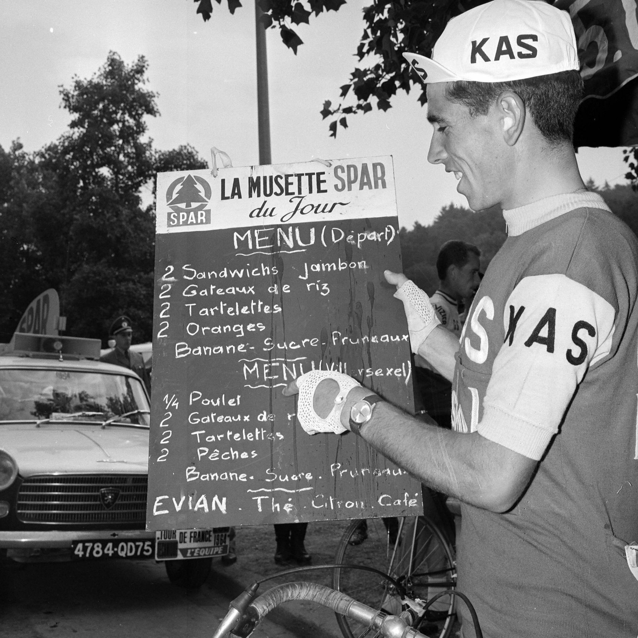 A Tour de France rider examines a blackboard of food options at the 1964 Tour