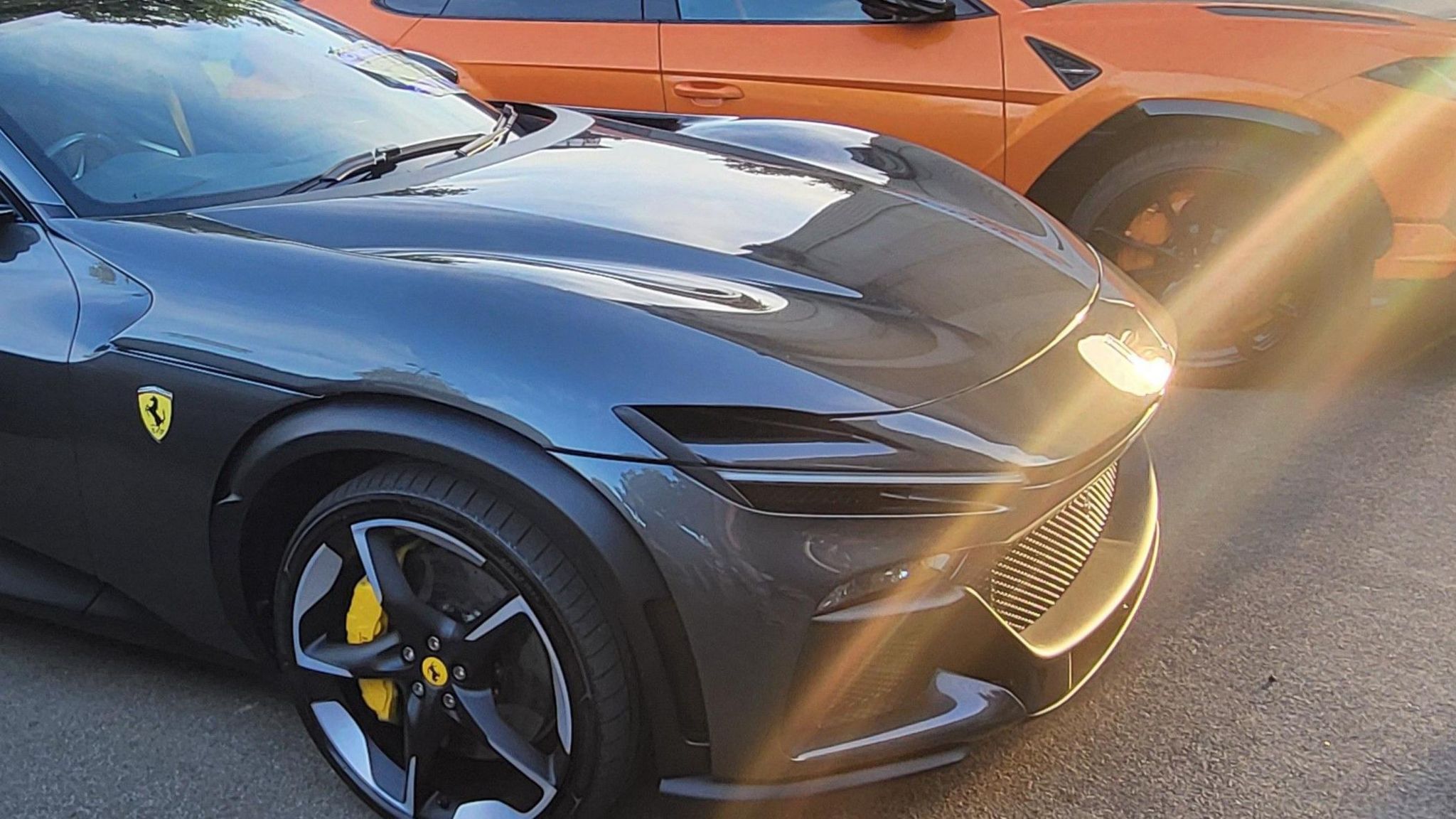 Close up of a black Ferrari's bonnet and front right wheel with sun streaks shining across it