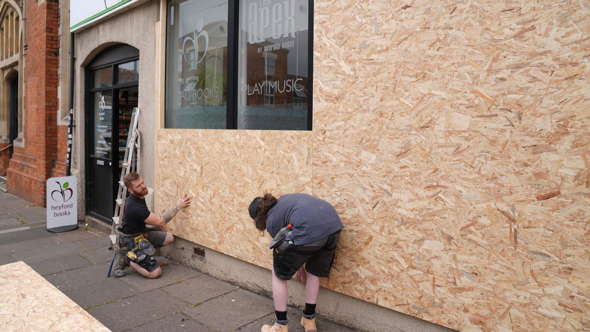 Two workmen placing boards over some windows 