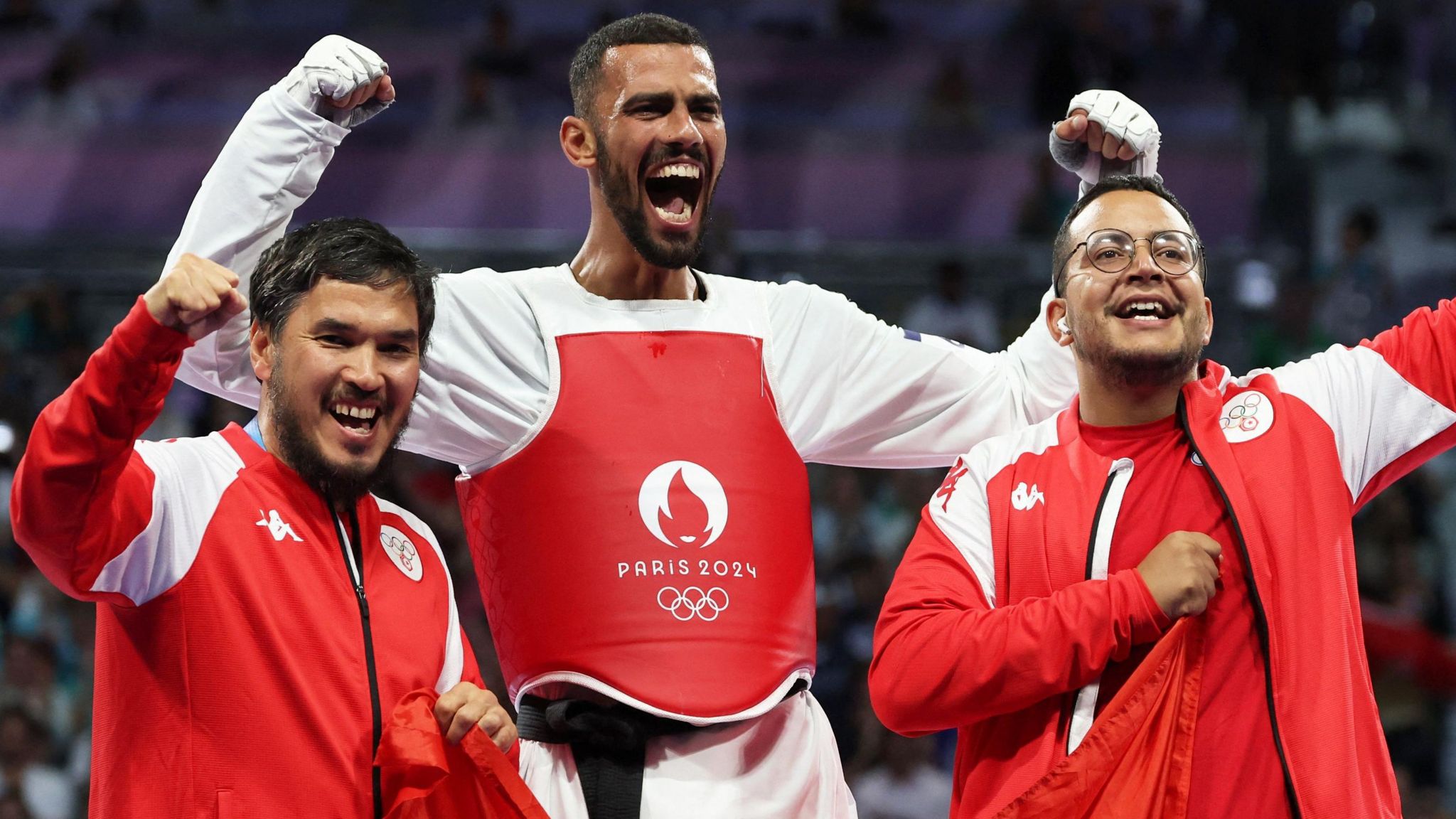 Firas Katoussi (centre) celebrates with two Tunisian support staff after winning gold at Paris 2024