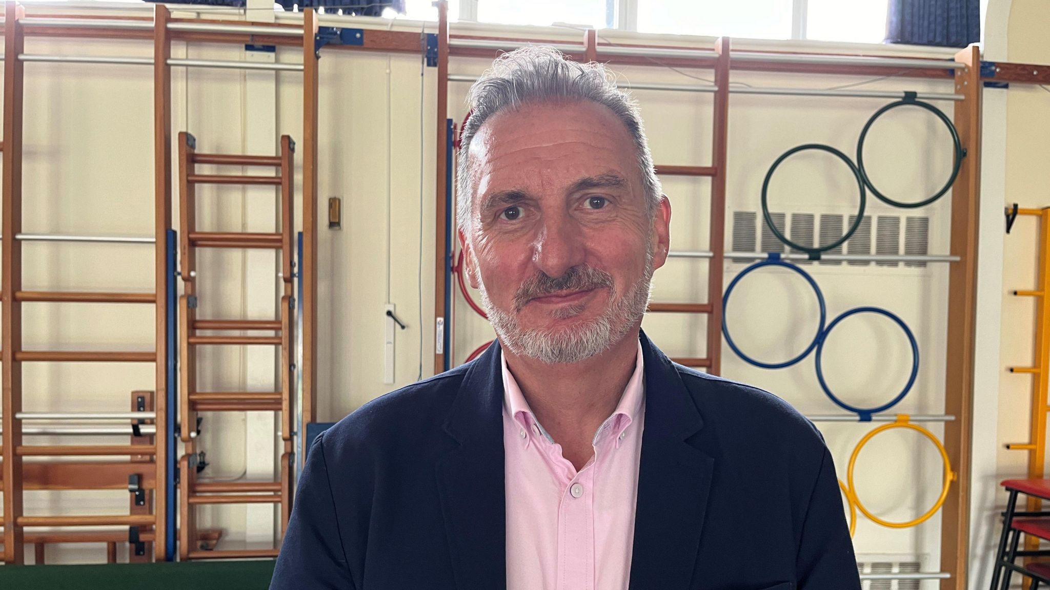 Jonathan in a school hall with wall-mounted gym equipment in the background