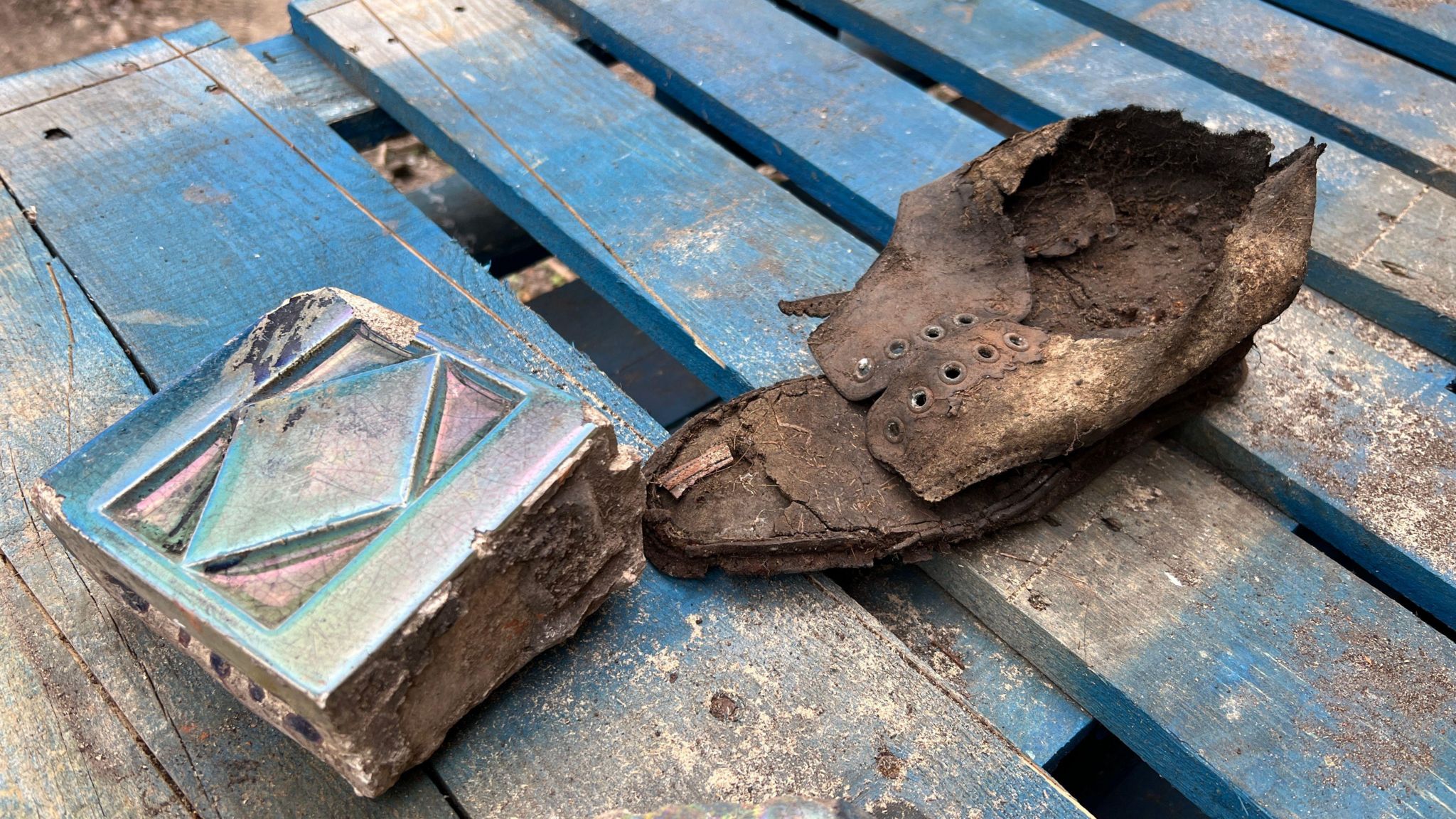 A rotten shoe and part of a blue decorative tile sit on top of a wooden pallet