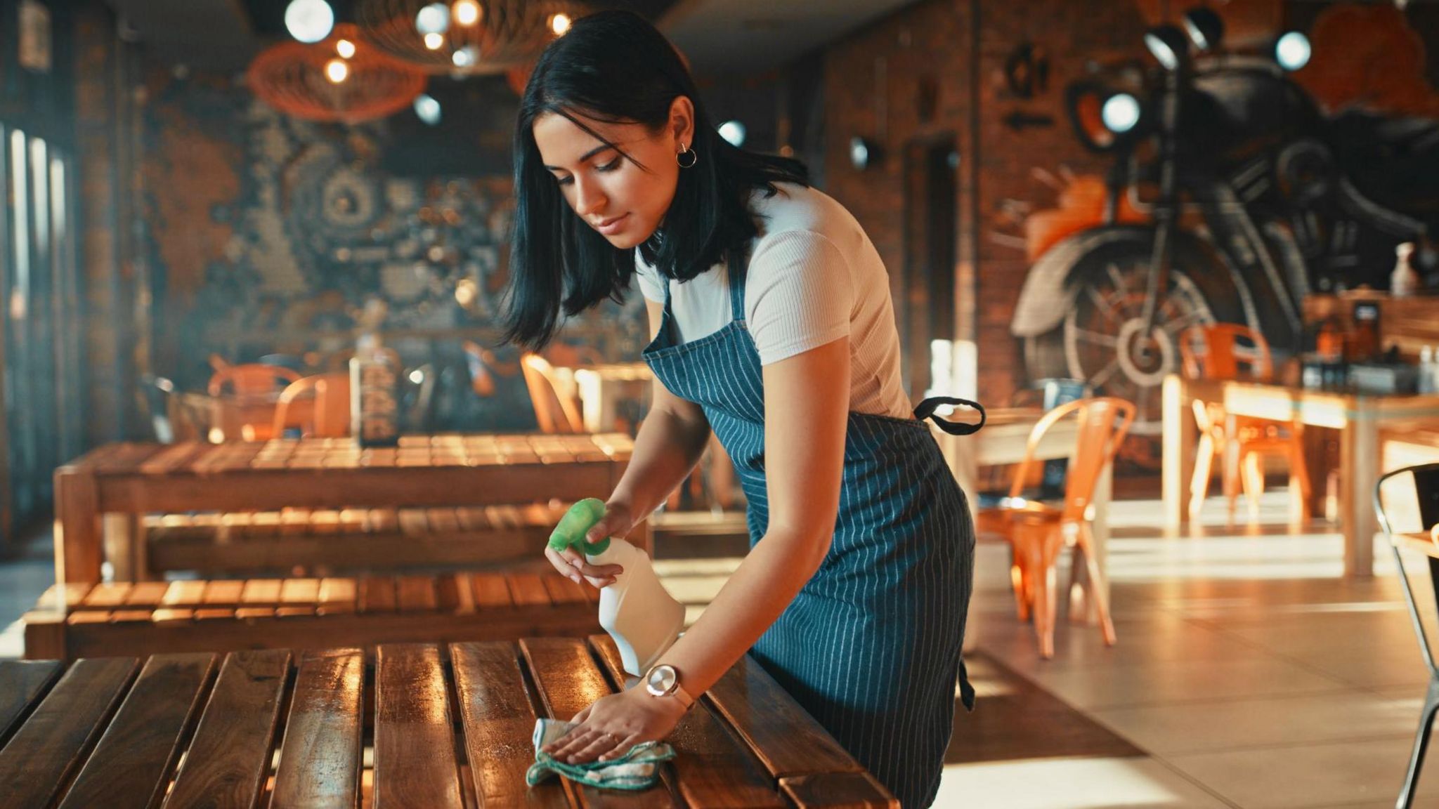 A young woman with dark hair working in cafe, cleaning a table