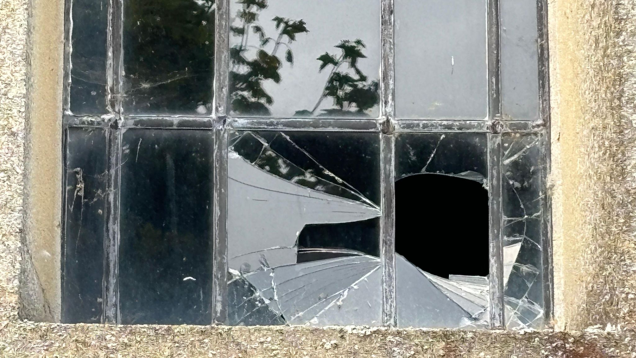 A smashed window of an old building is pictures, with two panes smashed 