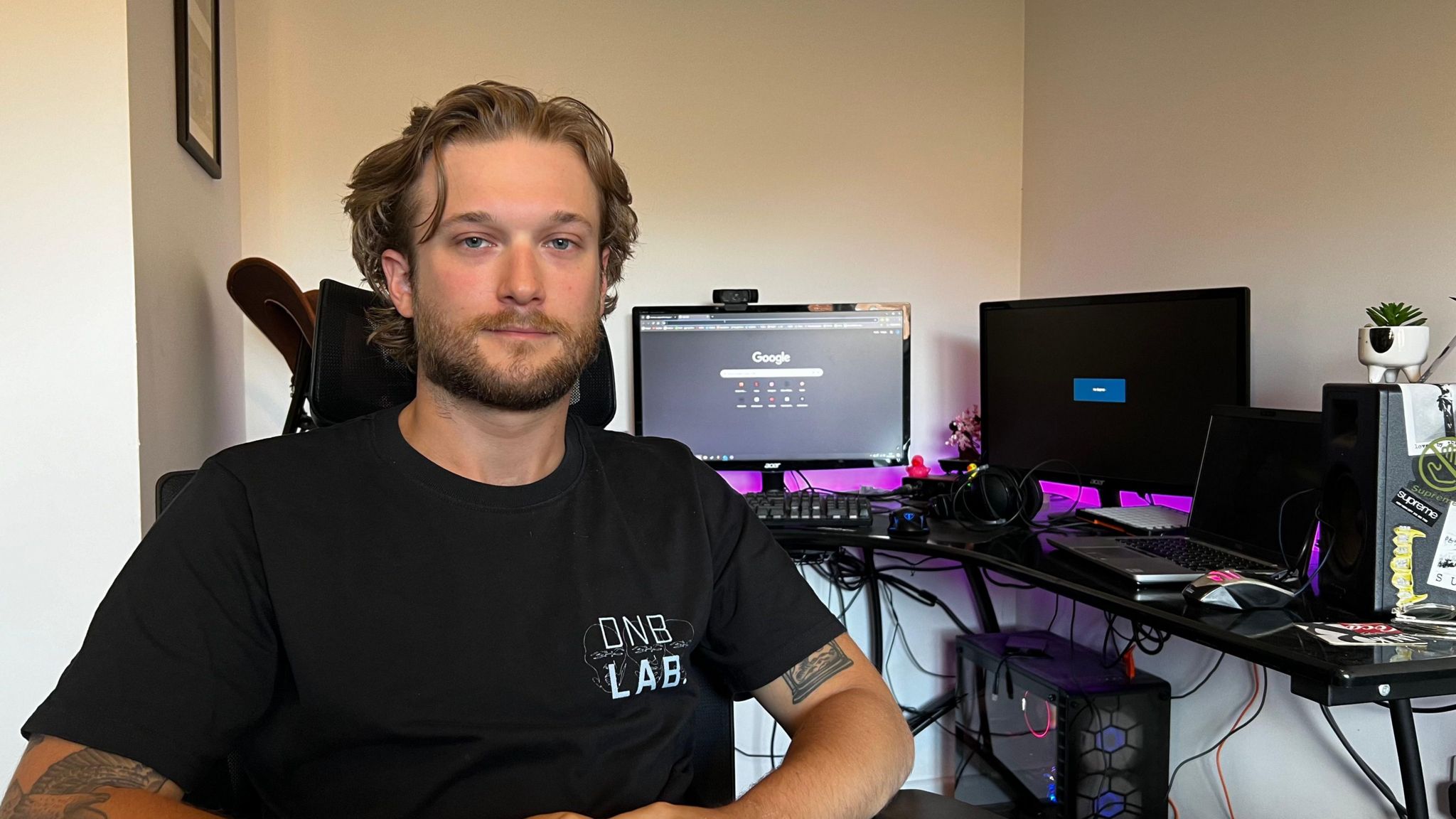 Jacob Derrick sitting down in a room. There are computer screens and a hard drive visible behind him