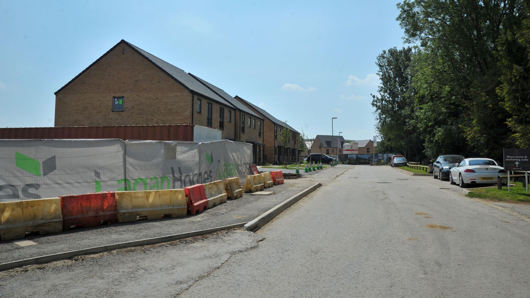 Lagan Homes site on Marlborough Road. A fence can be seen around the development and some new houses can be seen in the distance behind it. There are also flags for Lagan Homes along the path. 