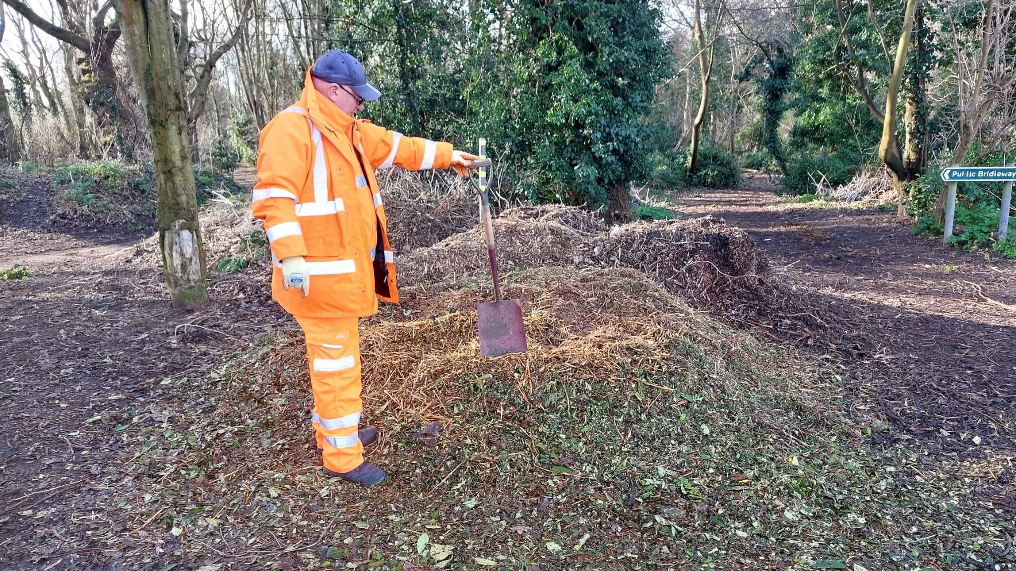 A council worker next to a dumped pile of garden waste