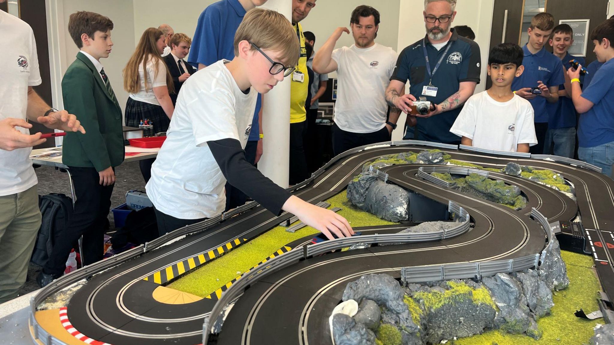 Child places a toy car onto a racing track with adults and children watching