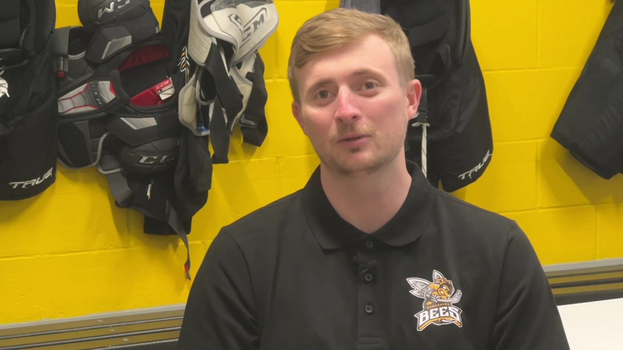 Stuart Mogg, a Berkshire Bees player, has short blonde/ginger hair and is wearing a black, buttoned T-shirt with the Berkshire Bees logo