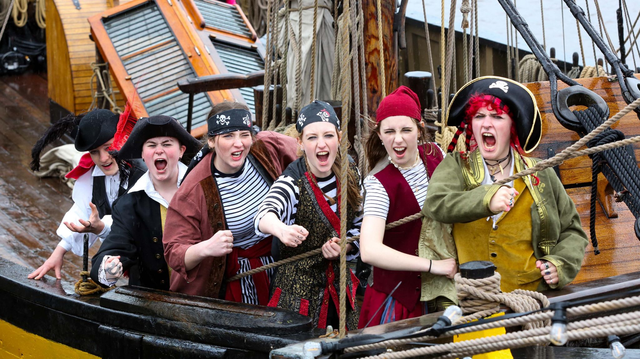 Six people dressed as pirates stand on the side of a pirate ship