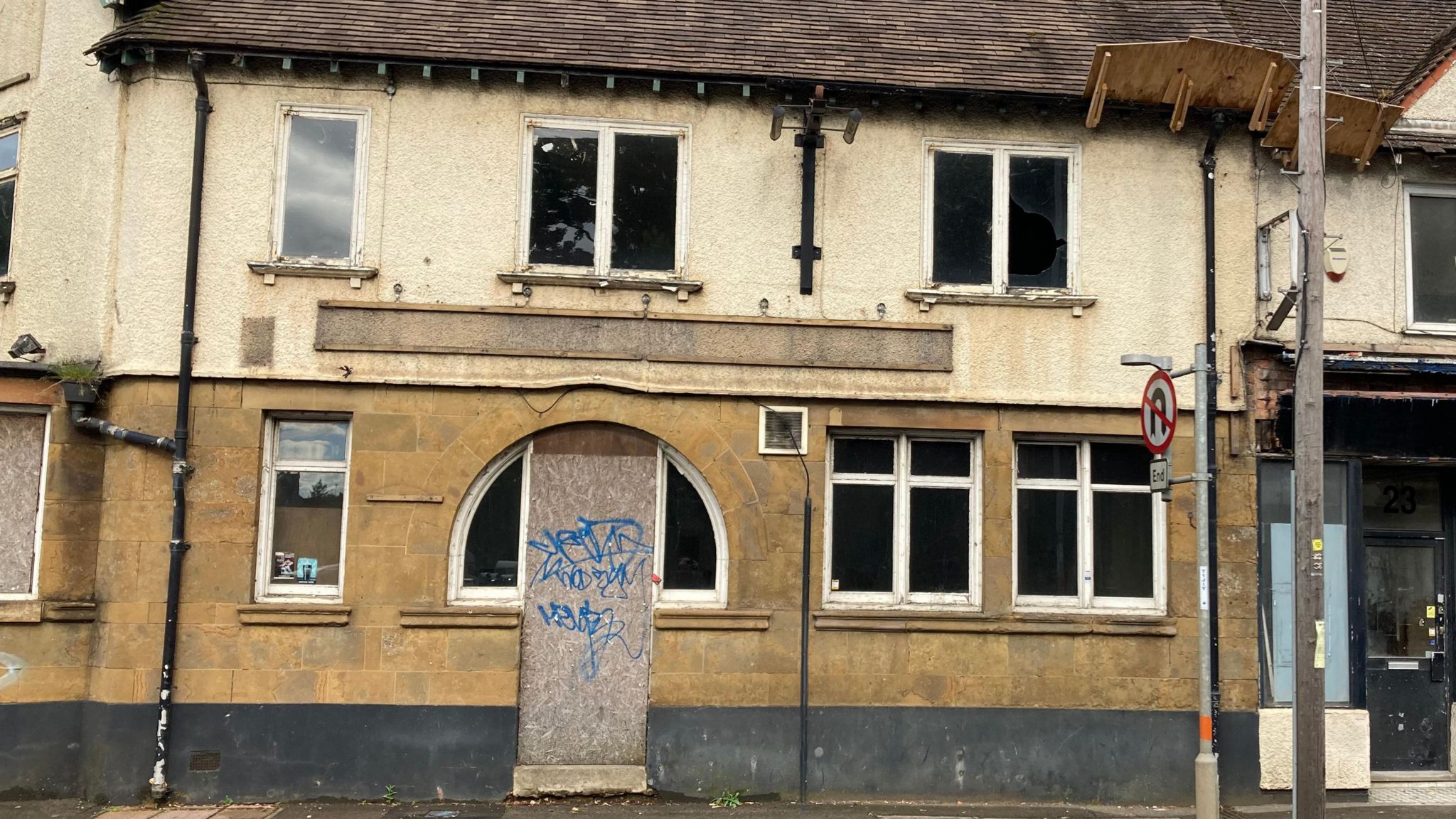 One facade of pub showing boarded up door with graffiti
