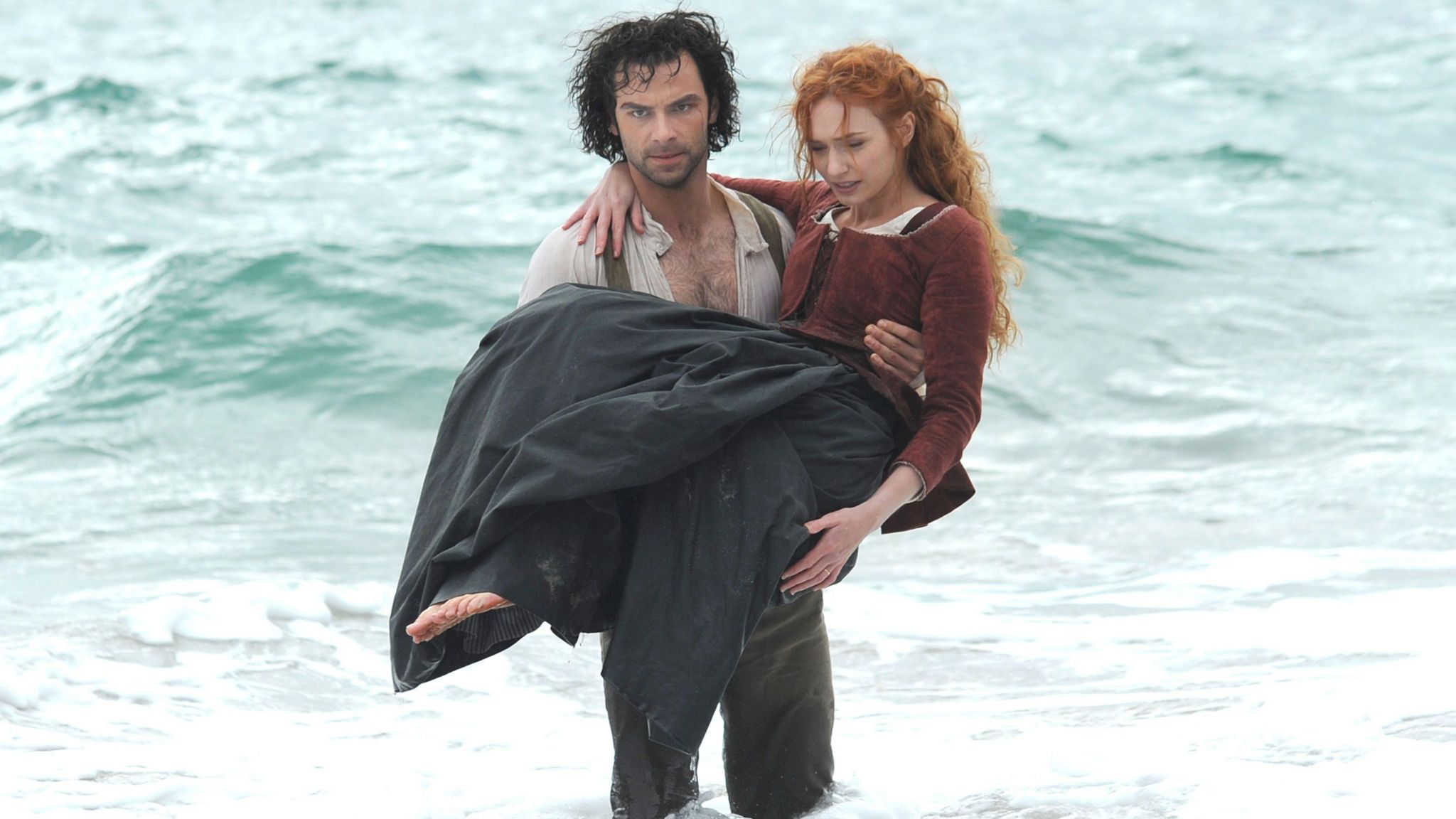 Aidan Turner as Ross Poldark in the sea holding Eleanor Tomlinson as Demelza in his arms in the BBC TV series Poldark