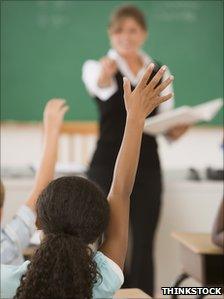 Students in a classroom raise their hands to answer the teacher's question