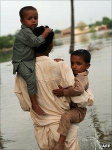 Pakistani villager carries two boys as he walks through water in Baseera