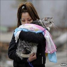 Woman holding pet cat in a tsunami devastated street in Japan