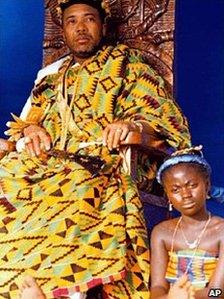 Liberian President Charles Taylor sits on a throne with a traditional dancer sitting at his feet during a ceremony in Monrovia where Ghanaian immigrants crowned him Chief Okatakyie The Greatest of Warriors - February 1998