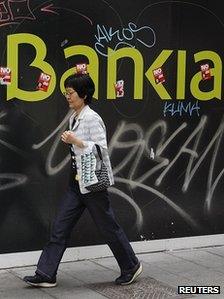 Woman walks past defaced Bankia sign in Madrid