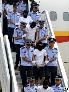 Hooded and hand-cuffed suspects are escorted to get off a plane after arriving in Beijing August 25