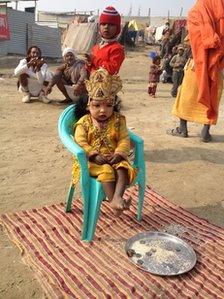 Child dressed as Hindu god sits in front of plate with money on it