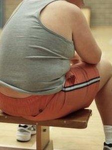 An overweight boy sits on a gym bench